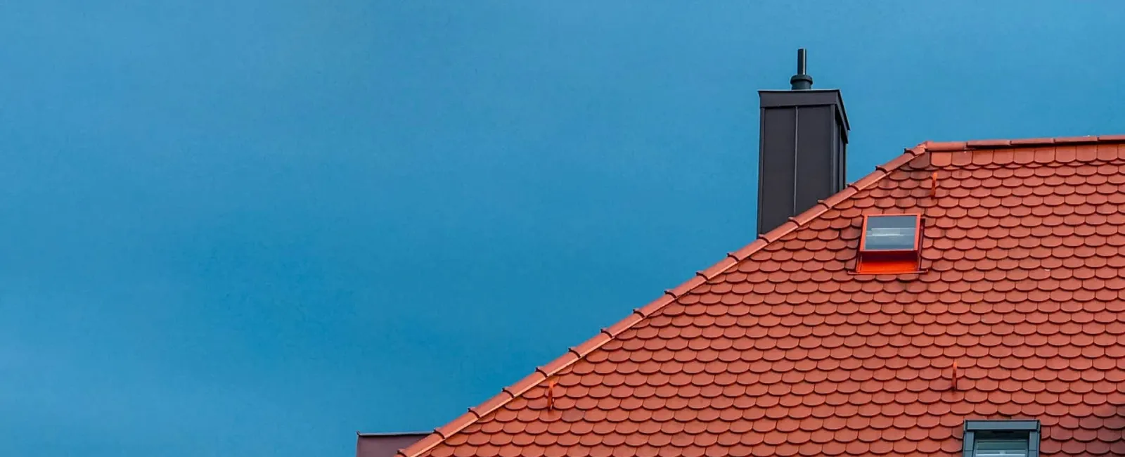 Red tile roof with a chimney against a blue sky