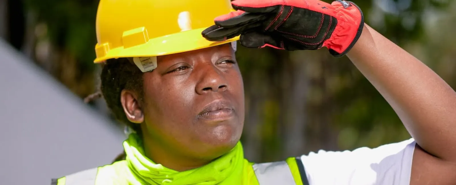 Construction worker in a hard hat and safety vest shading their eyes