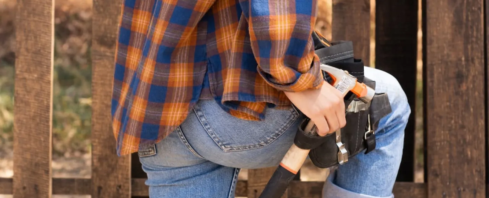 Worker in a plaid shirt wearing a tool belt beside wood framing