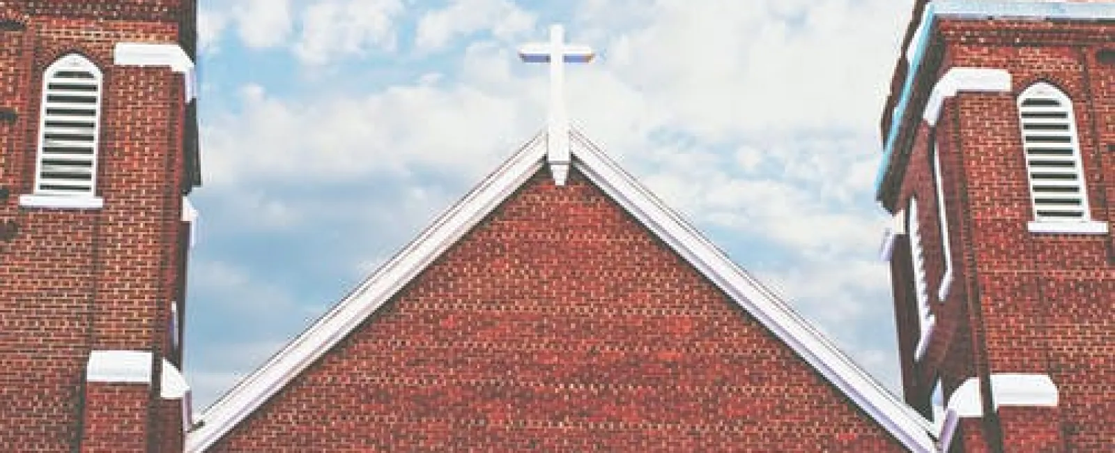 Brick church gable with a cross between two bell towers