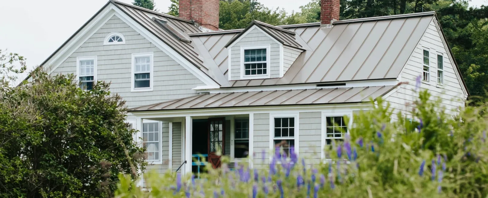 Gray home with a standing seam metal roof and lavender in front